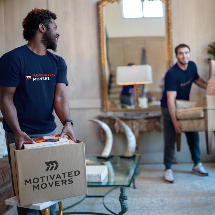 A few team members at Motivated Movers carefully lift a chair while another packs a customer's belongings into a moving box.